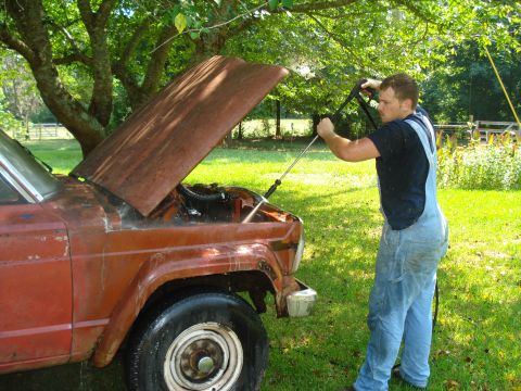 1984 Jeep J-10 - Pressure washing the engine bay of a 1984 Jeep J-10 in a grassy yard.