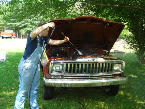 1984 Jeep J-10 - A person is cleaning the engine compartment of a Jeep truck with a pressure washer outdoors.