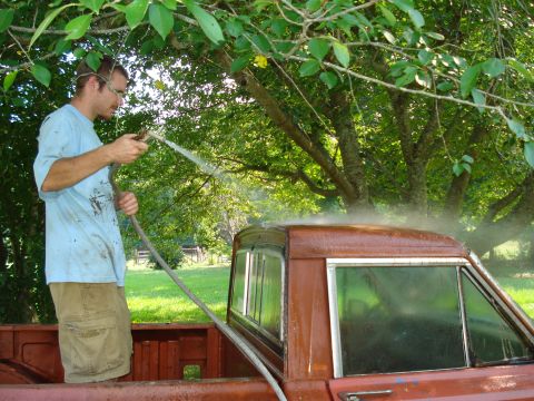 1984 Jeep J-10 - A man washes the side of a brown 1984 Jeep J-10 truck cab under a tree.