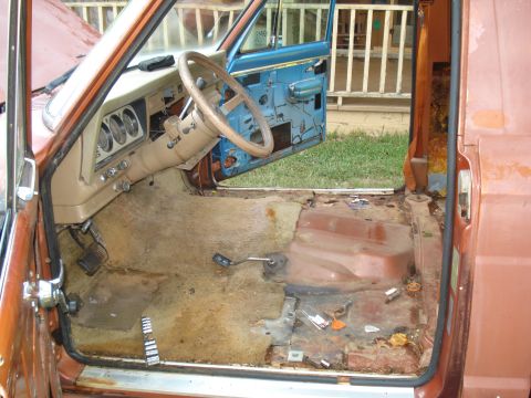1984 Jeep J-10 - The interior of a Jeep shows its dashboard, steering wheel, and floor, which is in rough condition.