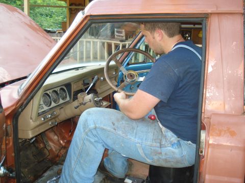 1984 Jeep J-10 - A man sits in the driver's seat of a 1984 Jeep J-10, working on the steering column. The dashboard gauges are visible.