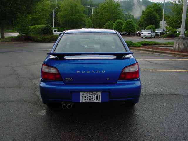 Rear of blue Subaru WRX sedan with dual exhaust and NC plate in a parking lot