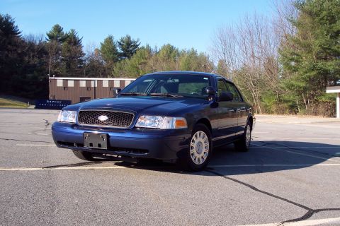 2001 Ford Crown Victoria - A blue sedan is parked in an empty lot on a clear day, with trees and a building in the background.