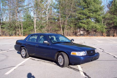 2001 Ford Crown Victoria - A dark blue 2001 Ford Crown Victoria is parked in an empty lot on a sunny day.