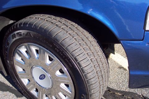 2001 Ford Crown Victoria - Close-up of a blue 2001 Ford Crown Victoria's front wheel and fender, showing the tire and a Ford logo on the hubcap.