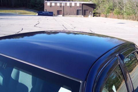 2001 Ford Crown Victoria - A dark blue sedan's roof and side are visible, with a dumpster in the background of an empty parking lot.