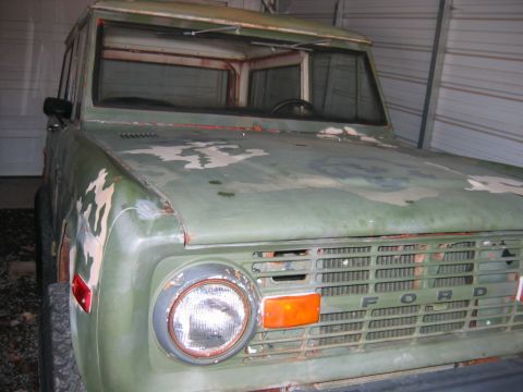 1992 Ford Mustang - Close three-quarter front view of an early Ford Bronco in faded green camouflage paint parked under a metal carport, with doors removed and…
