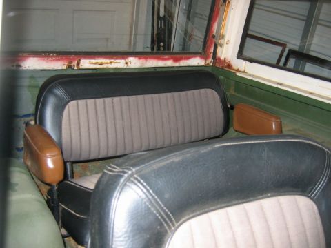 1992 Ford Mustang - Interior of a stripped vintage vehicle showing black-vinyl and gray-ribbed-cloth bench seats with tan padded armrests sitting on a bare, un…