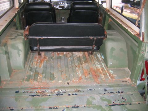1992 Ford Mustang - Looking rearward into the stripped rear cargo area of an early Ford Bronco-style body, showing a ribbed steel floor with heavy surface rust…