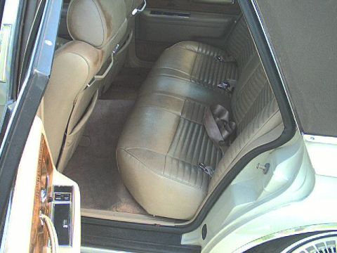 1987 Lincoln Continental - The interior of a car shows a tan bench seat with seatbelts and a portion of the door panel.