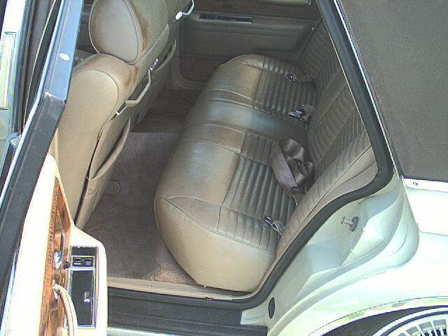 Tan leather rear bench seat interior of a sedan with worn upholstery