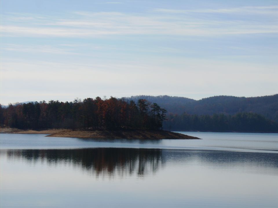 Calm lake with a wooded peninsula and hills in winter