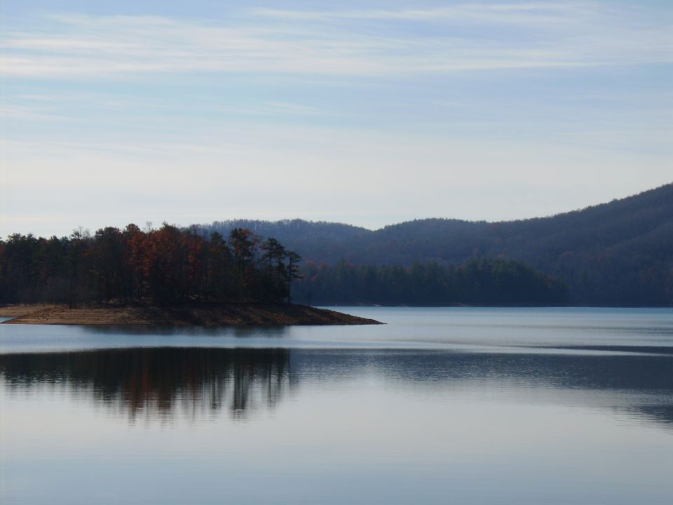 Still lake with forested point and mountains at dusk