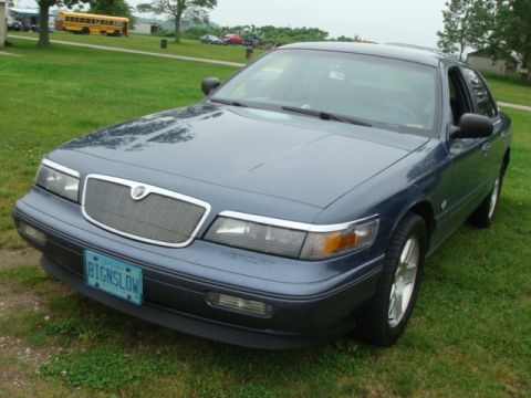 2004 Ford Crown Victoria - A blue Mercury Grand Marquis is parked on a grassy area with a yellow school bus in the background.