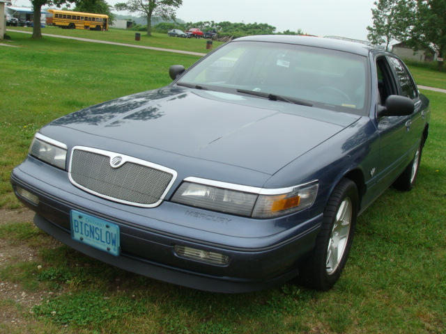 Blue Mercury Grand Marquis parked on grass. License plate reads BIGNSLOW. Text 'MERCURY' visible on the front fender