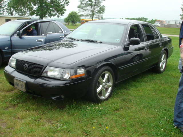 Black 2004 Ford Crown Victoria sedan, 3/4 front view. Another blue sedan is parked to the left