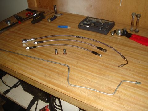 1992 Ford Bronco - Various brake lines and tubing are laid out on a wooden workbench alongside tools and hardware.