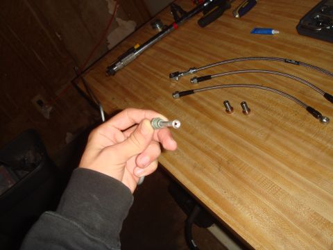 1992 Ford Bronco - A person holds a brake line fitting, with new brake lines and other parts laid out on a table.