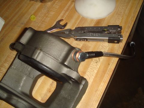 1992 Ford Bronco - A brake caliper and a multi-tool are laid out on a wooden table, possibly for repair or maintenance.