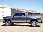 2002 Dodge 2500 - Side view of a two-tone Dodge Ram pickup truck parked in a dry, dusty area with farm buildings in the background.