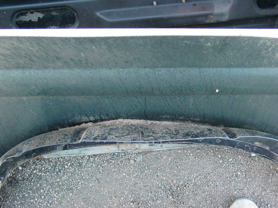 Dark green vehicle wheel well with gravel and a damaged black fender flare