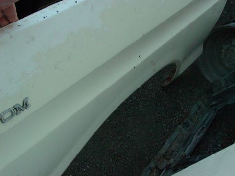 1979 Ford Bronco - A partial view of a vehicle's fender and wheel well shows a chrome emblem and the textured surface of the body panel.