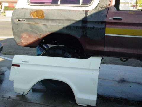 1979 Ford Bronco - A white fender panel is positioned next to a damaged maroon and black Ford Bronco with a yellow stripe.