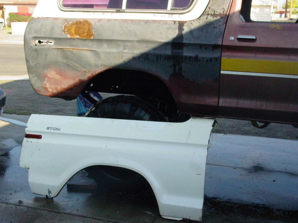 White fender panel attached to a maroon and black Ford Bronco with yellow stripe, showing rust and damage