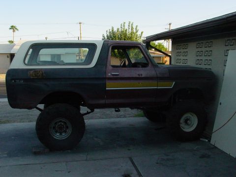 1979 Ford Bronco - This lifted 1979 Ford Bronco is seen in a driveway with a white camper shell and a distinctive yellow stripe on its side.