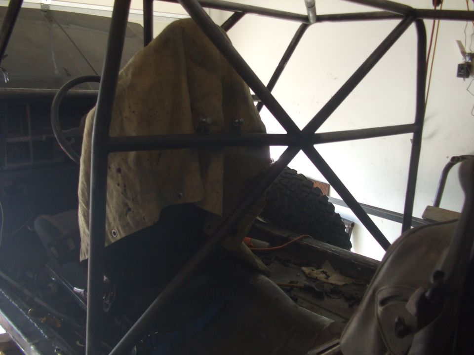 Interior of a vehicle with a custom roll cage, tarp-covered seat, and spare tire visible