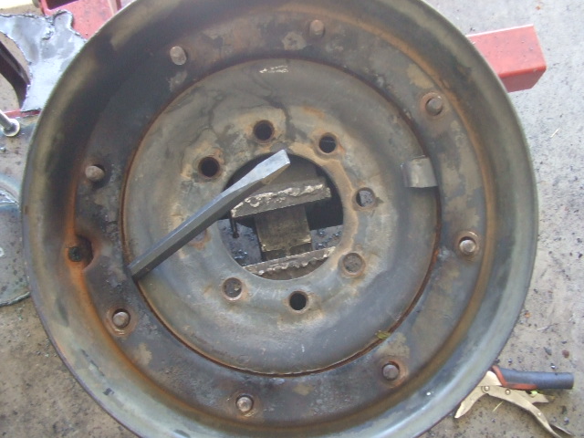 Rusty wheel rim with a chisel inserted and a vise gripping the center hub