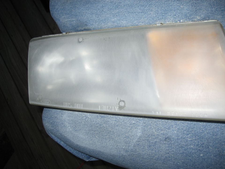 Removed Ford headlamp lens with amber corner section and molded part number 13U21V on denim fabric