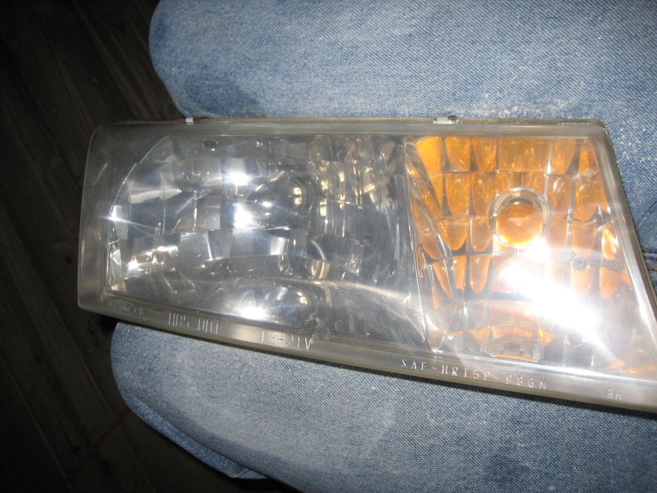 Removed RH headlight assembly with clear lens and amber turn signal section, resting on jeans