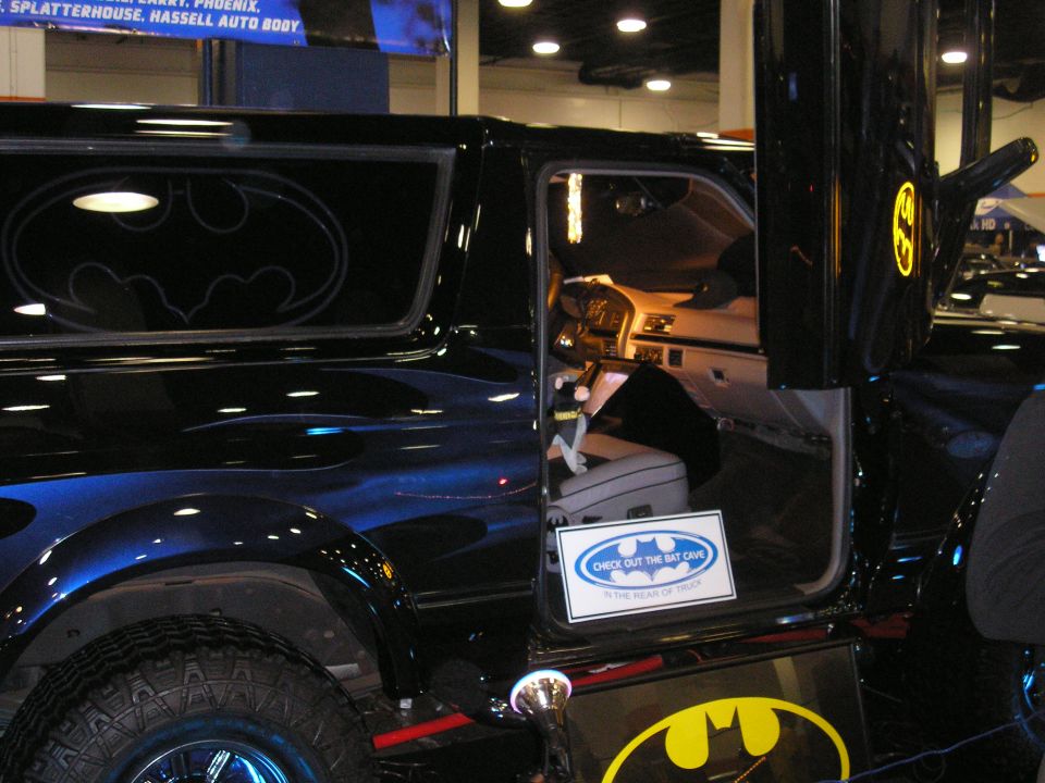 Black Batman-themed show truck with blue ghost flames and bat logos at an indoor auto show