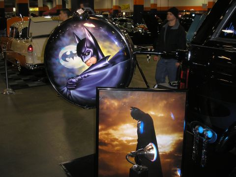 1995 Ford Bronco - A display Batman-themed art alongside vehicles at an indoor event.