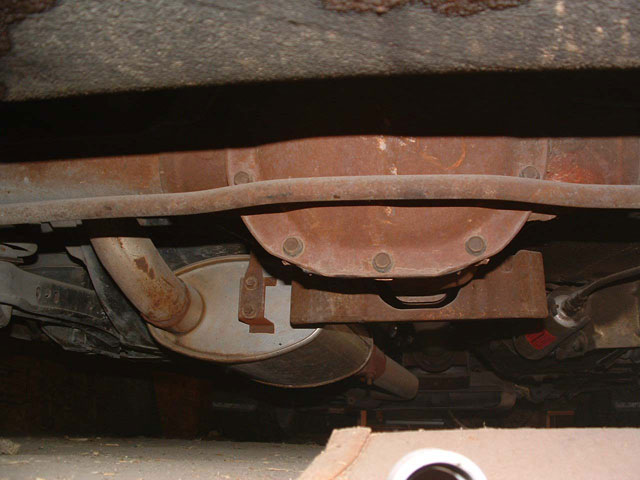 Rusty rear axle differential cover, leaf spring and muffler seen from under a car