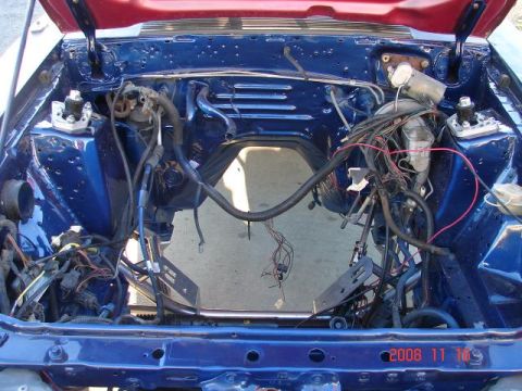 1985 Ford Mustang - The engine bay of a 1985 Ford Mustang shows exposed wiring and components, indicating it is undergoing maintenance or restoration.