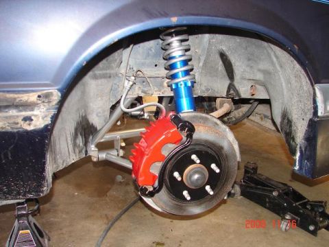 1985 Ford Mustang - Close-up of the front wheel assembly on a 1985 Ford Mustang, a red brake caliper and blue coilover suspension.