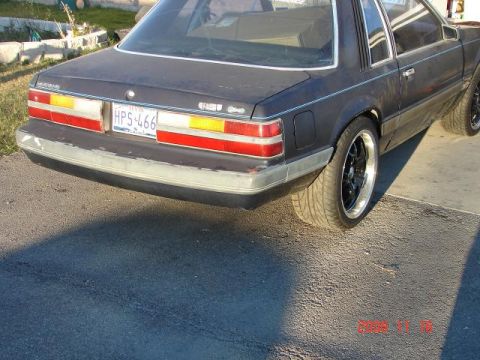 1985 Ford Mustang - The rear of a dark-colored Ford Mustang is shown, its taillights and license plate.