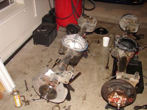 1985 Ford Mustang - Disassembled rear axles and parts are laid out on a garage floor.