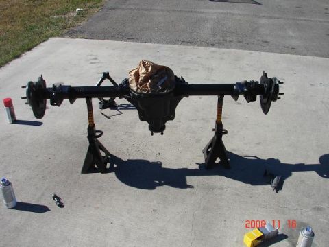 1985 Ford Mustang - A rear axle assembly is shown on jack stands, with two spray cans and a tool on the concrete surface.