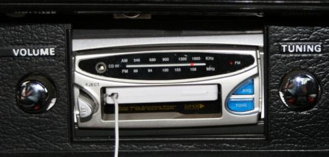 1976 Ford Ranchero - Close-up of a car's interior showing a stereo system with volume and tuning controls, a CD player, and auxiliary input.