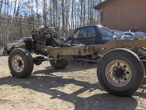 1990 Ford Bronco - A disassembled truck chassis sits outdoors with its engine exposed, while another vehicle is visible in the background.