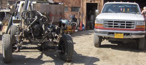 1990 Ford Bronco - A white Ford pickup truck is parked next to a vehicle chassis in a yard. The truck's grille suggests an early 1990s model.