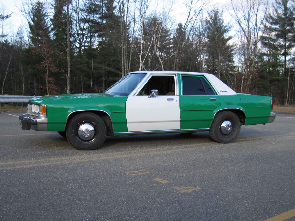 Driver-side profile of green and white Ford sedan on a road