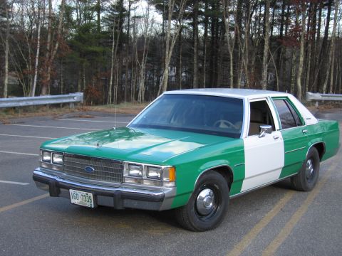1991 Ford LTD Crown Victoria - Green-and-white two-tone Ford sedan viewed from the front, with a New Hampshire plate reading 160 7339 and bare trees behind.