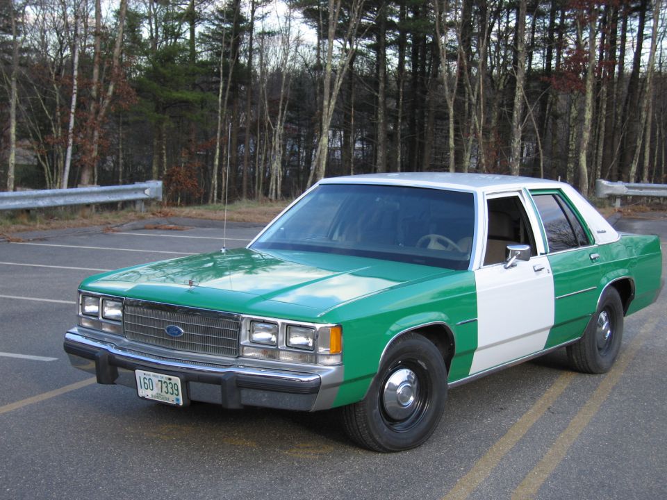Front of green and white Ford sedan parked on a road, NH plate