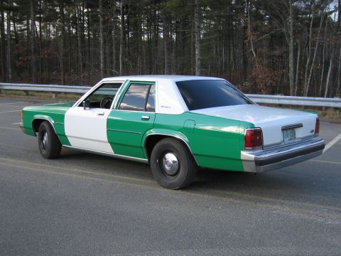 1991 Ford LTD Crown Victoria - green-and-white two-tone Ford sedan photographed from the rear driver side on a roadway lined with bare trees.