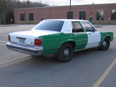 1991 Ford LTD Crown Victoria - Green-and-white two-tone Ford sedan shot from the rear passenger side in a parking lot before a brick building.
