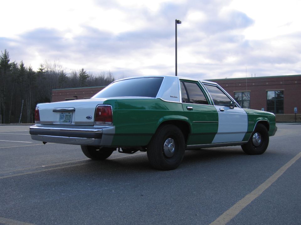 Rear three-quarter of green and white Ford sedan in a lot under cloudy sky